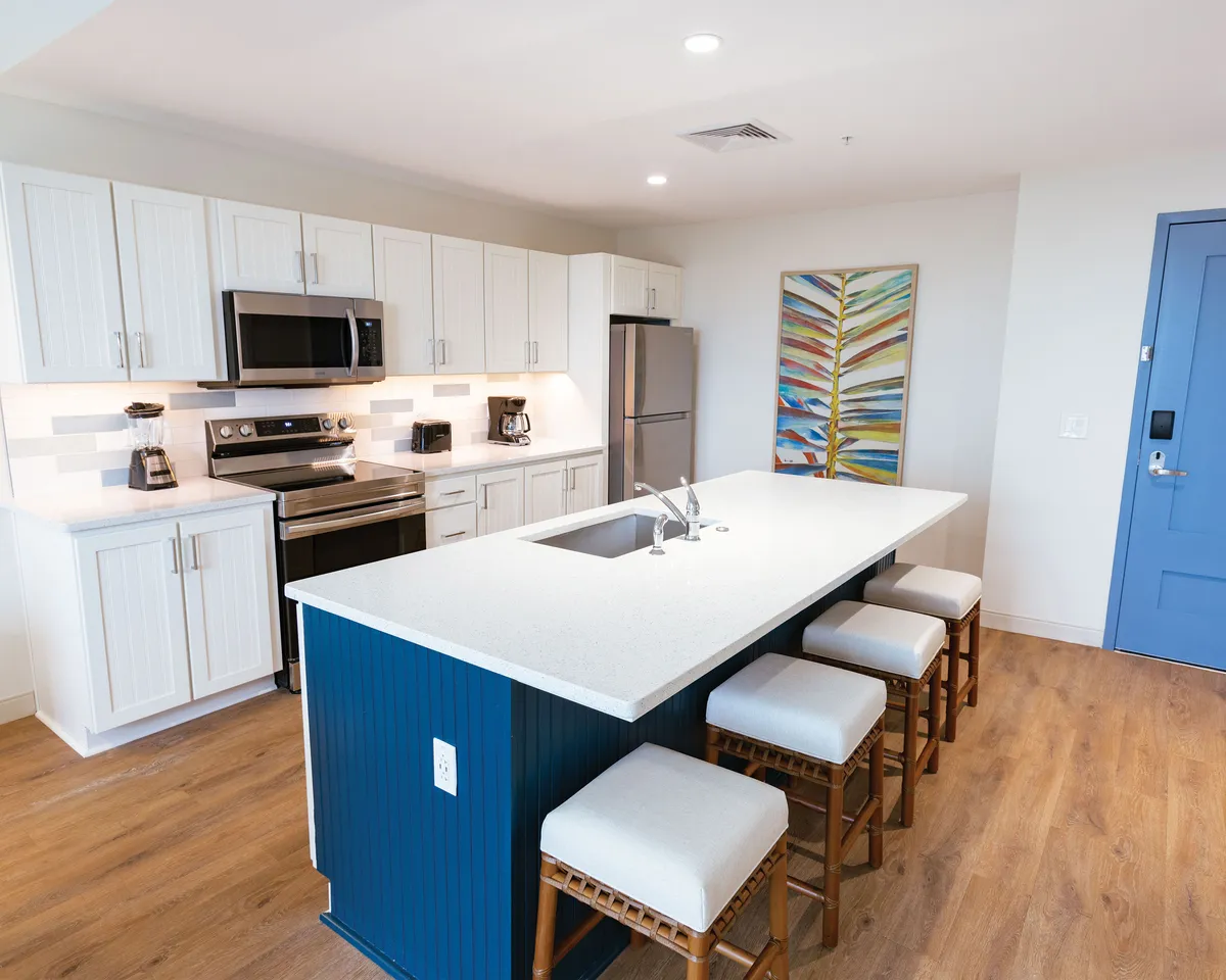 A close-up view of the kitchen area, focusing on a spacious island countertop, modern appliances, and colorful wall art. The setup encourages cooking, entertaining, and casual dining, aligning with the section’s emphasis on home-cooked meals and convenience.