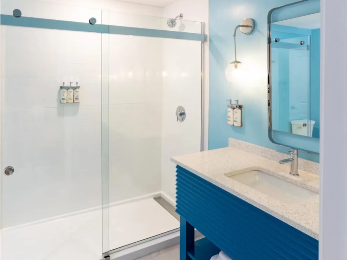 A modern bathroom with a glass walk-in shower enclosure, a refreshing blue accent wall, and a stylish textured countertop. The clean, spa-like environment encourages relaxation and rejuvenation.